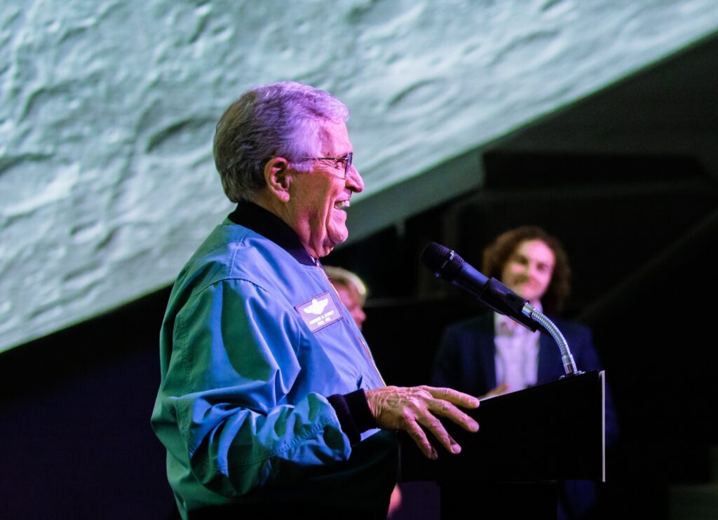 Speaker at a podium in front of a projected lunar surface